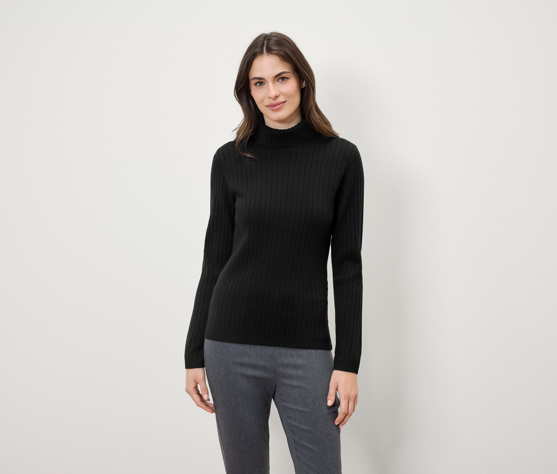 Frau trägt einen schwarzen Rollkragenpullover und graue Hosen.