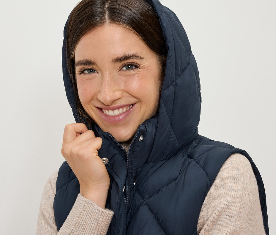 Lächelnde Frau trägt eine dunkelblaue Steppweste mit Kapuze.