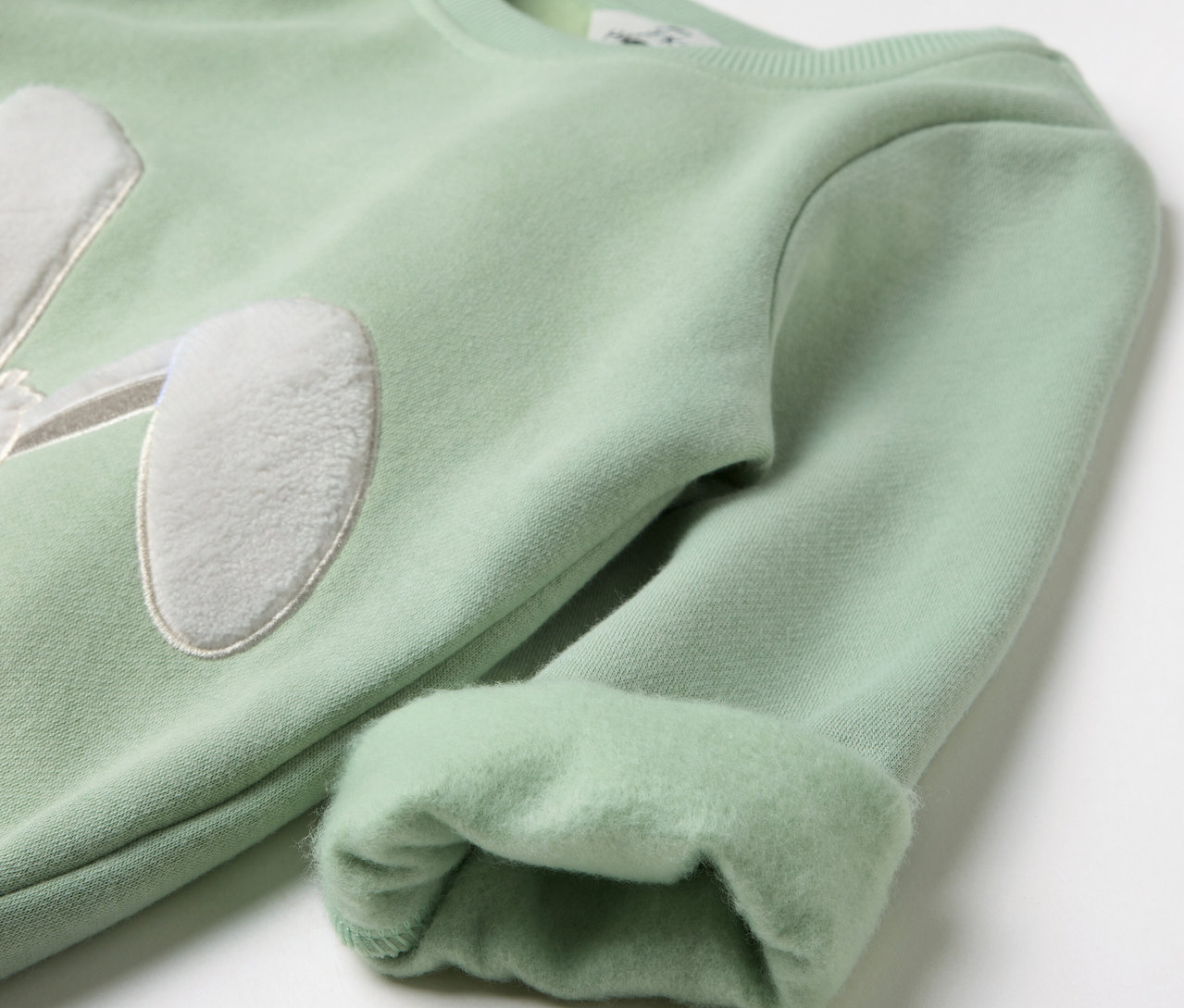 Hellgrüner Pullover mit Hasenohren-Applikation auf der Brust und hochgekrempelten Ärmeln.