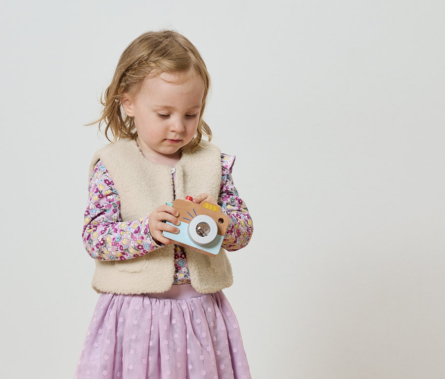 Ein kleines Mädchen mit blonden Zöpfen hält eine Spielzeugkamera.