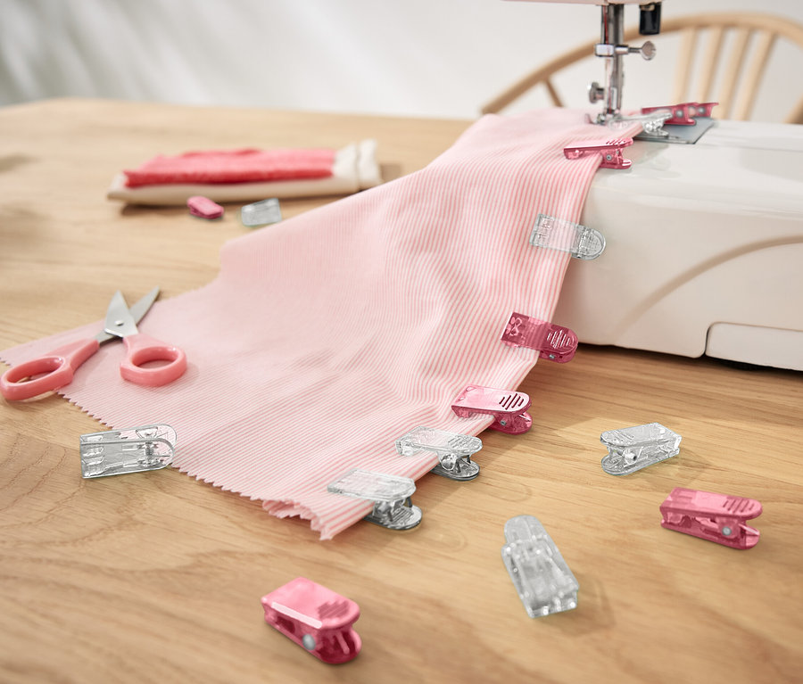 Rosa Stoff mit 20 Stoffklammern an einer Nähmaschine.