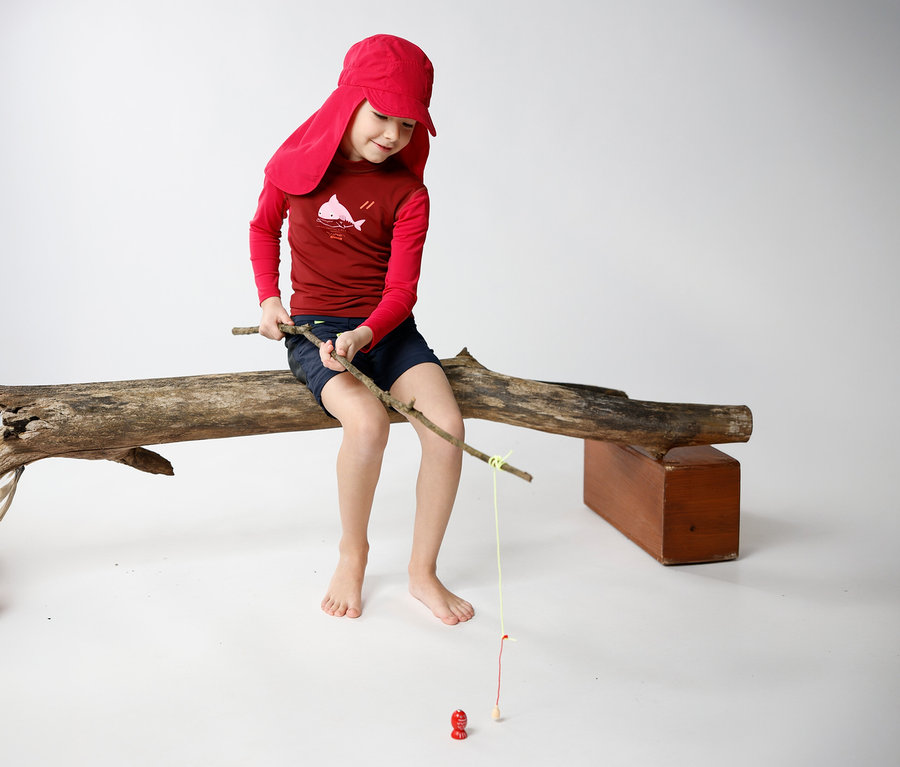 Junge sitzt mit JAKO-O Kappe mit Nackenschutz in Traube auf Baumstamm und angelt mit Stock.