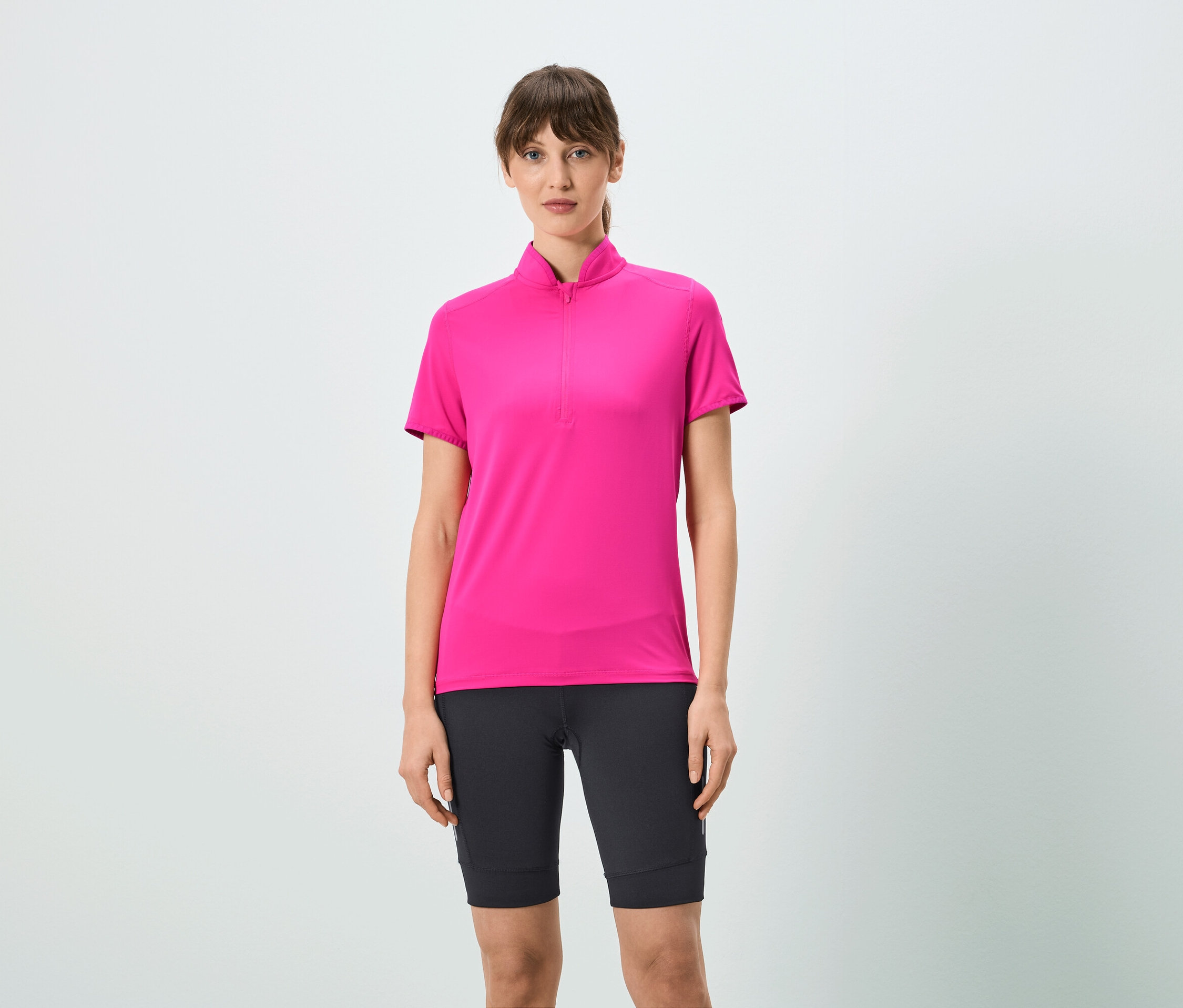 Frau trägt ein pinkes T-Shirt mit kurzem Reißverschluss und schwarze Shorts.