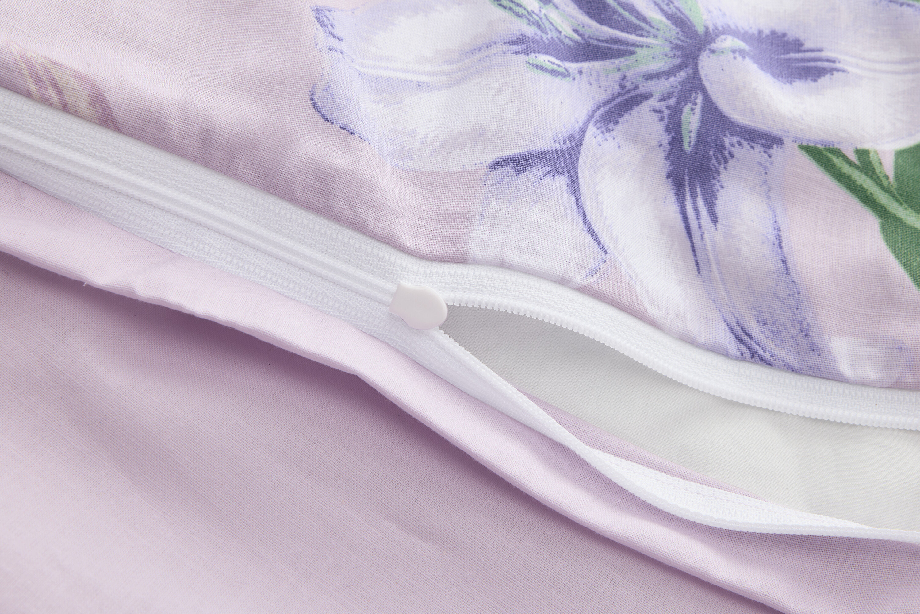 Nahaufnahme eines teilweise geöffneten lila Bettbezugs mit Blumendruck und Reißverschluss.