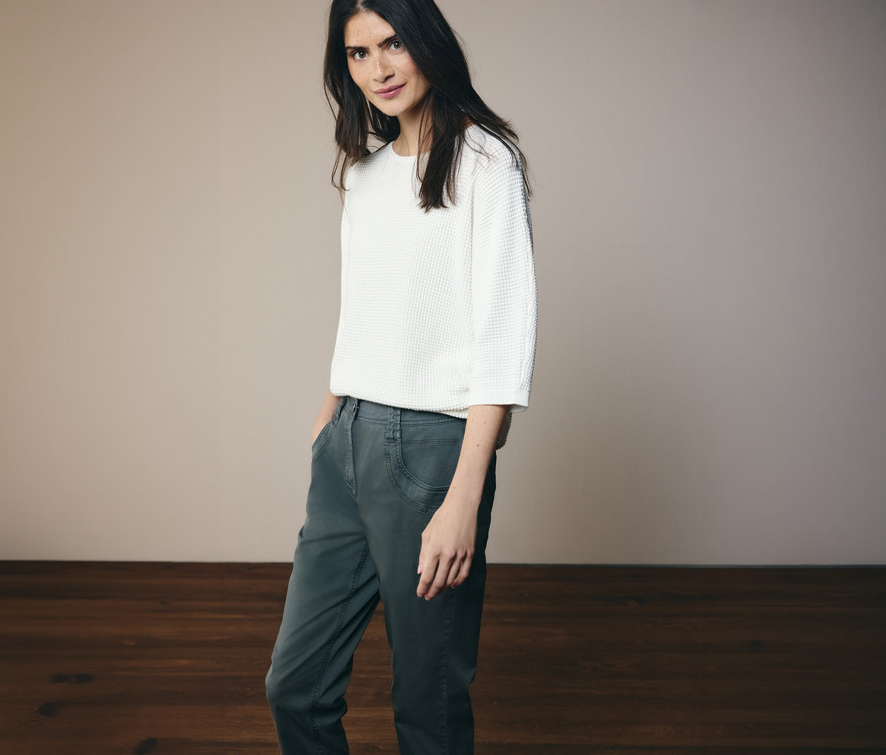 Frau mit weißem Oberteil und CECIL Hose »Scarlett« in dunklem Grün posiert vor hellem Hintergrund.