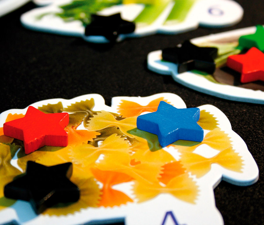 Nahaufnahme von Spielkarten mit Pasta-Motiven und farbigen Sternen aus dem Spiel »Welt der guten Küche«.