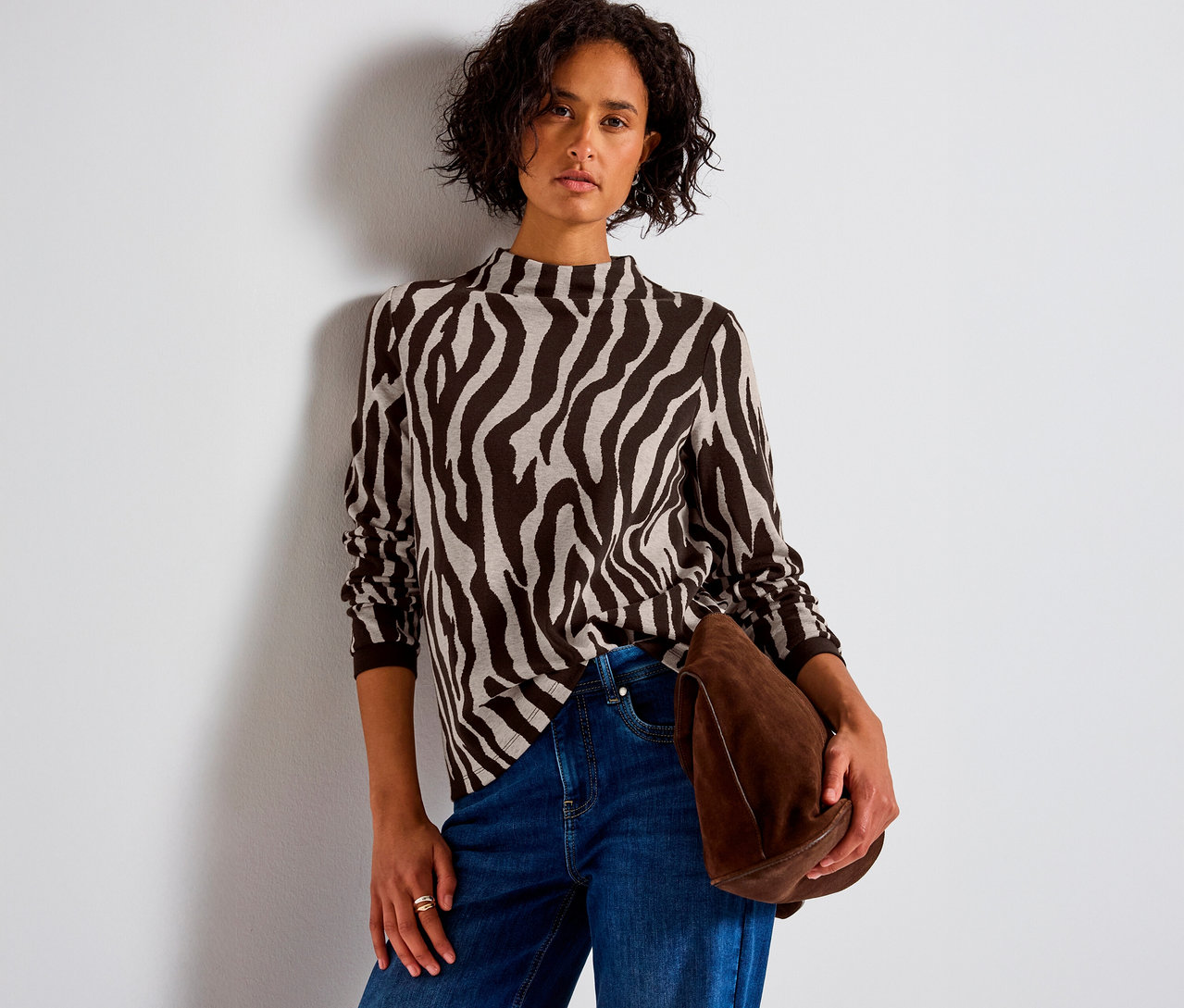 Frau trägt Street One Jacquard-Shirt mit Zebramuster, Jeans und hält eine braune Tasche.