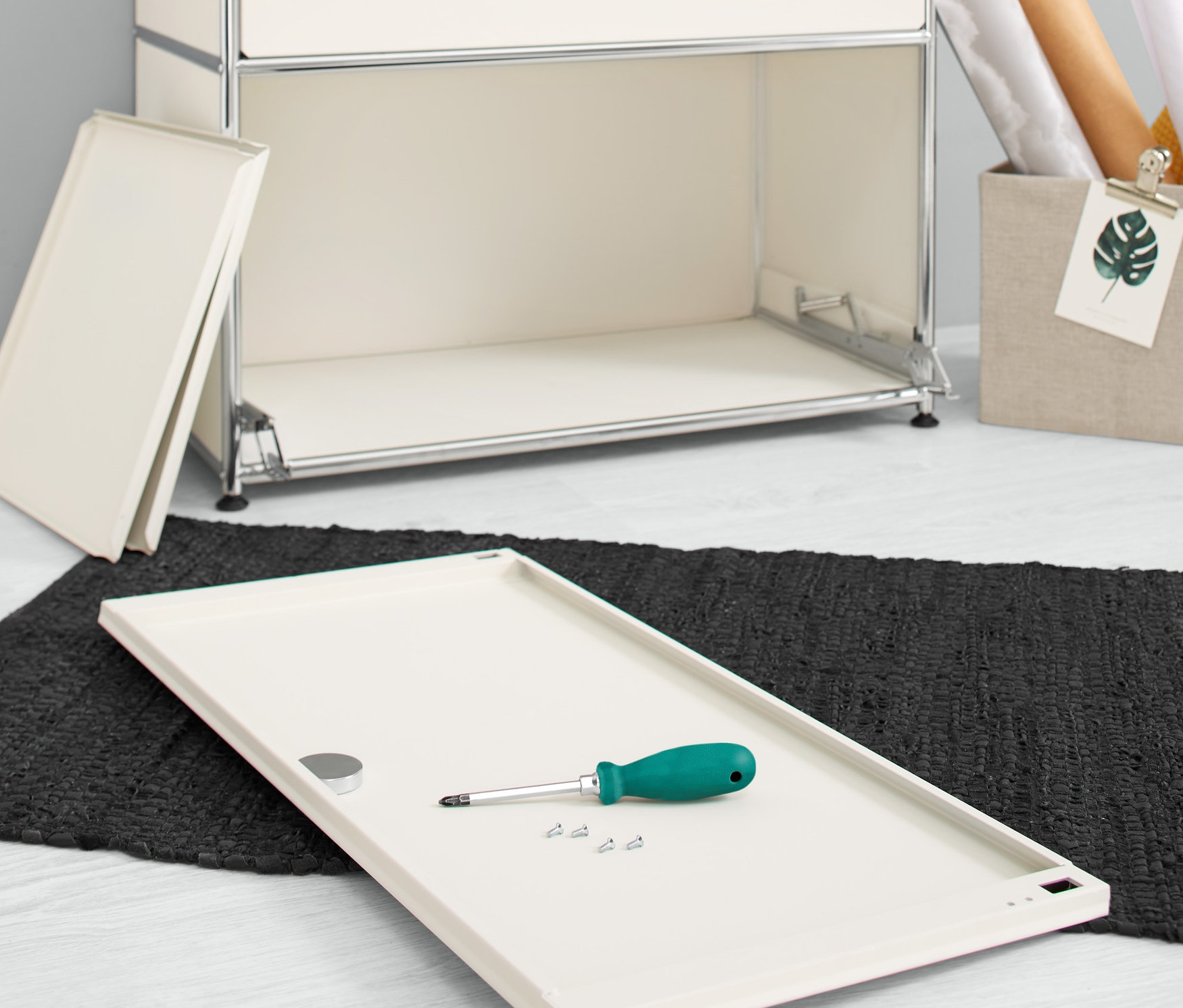 Ein weißes Klappenergänzungs-Set Metall »CN3« liegt mit Schraubenzieher und Schrauben neben einer Kommode auf dem Boden.