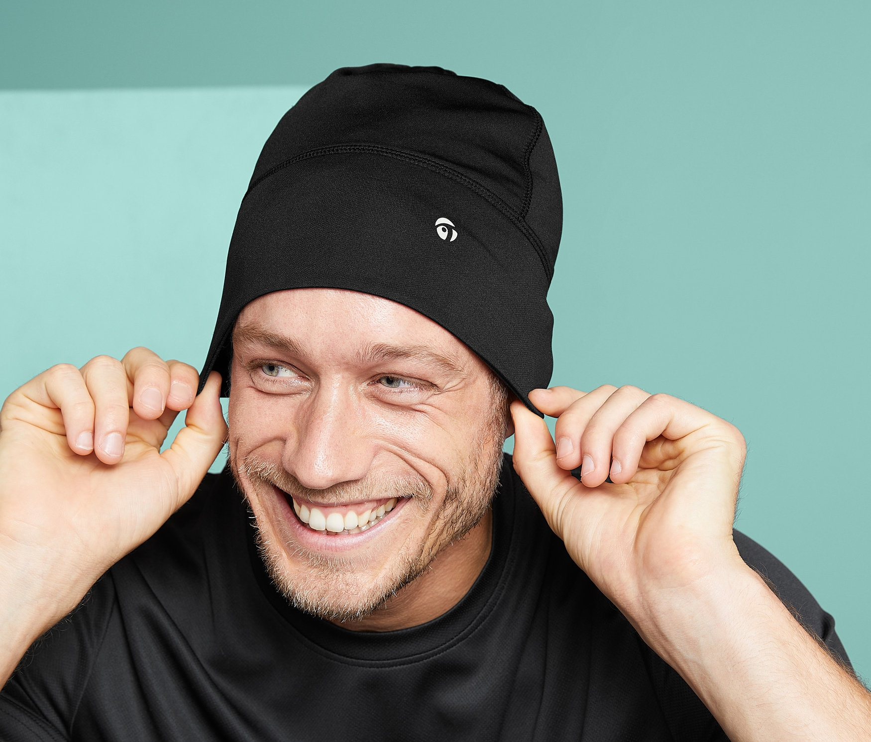 Mann lächelt und hält die Ränder seiner schwarzen Unisex-Funktionsmütze.