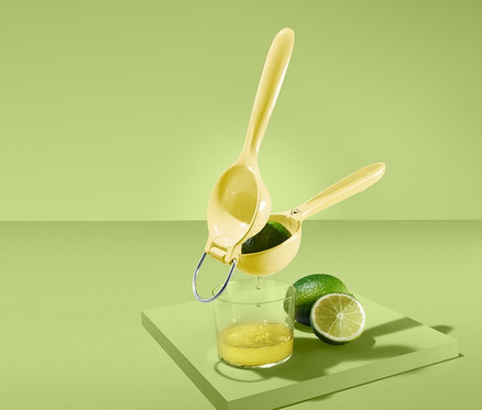 Eine gelbe Zitruspresse über einem Glas Saft und einer Limette auf grünem Hintergrund.