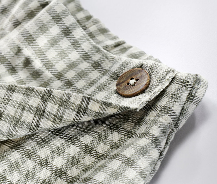 Detailaufnahme eines Kinder-Hosenrocks mit braunem Knopf und Karomuster.