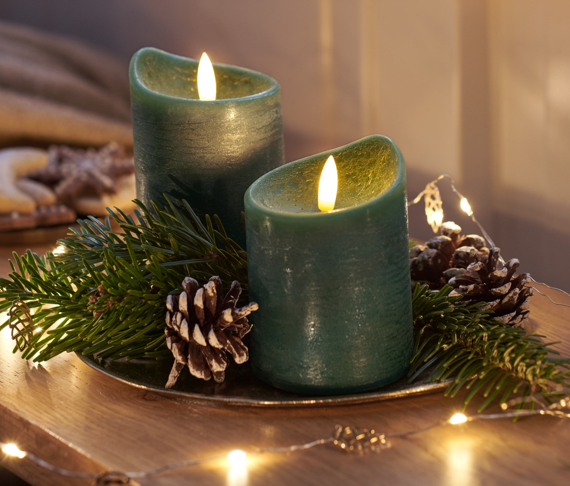 Zwei dunkelgrüne LED-Echtwachskerzen auf einem Dekoteller mit Tannenzapfen und Tannenzweigen.