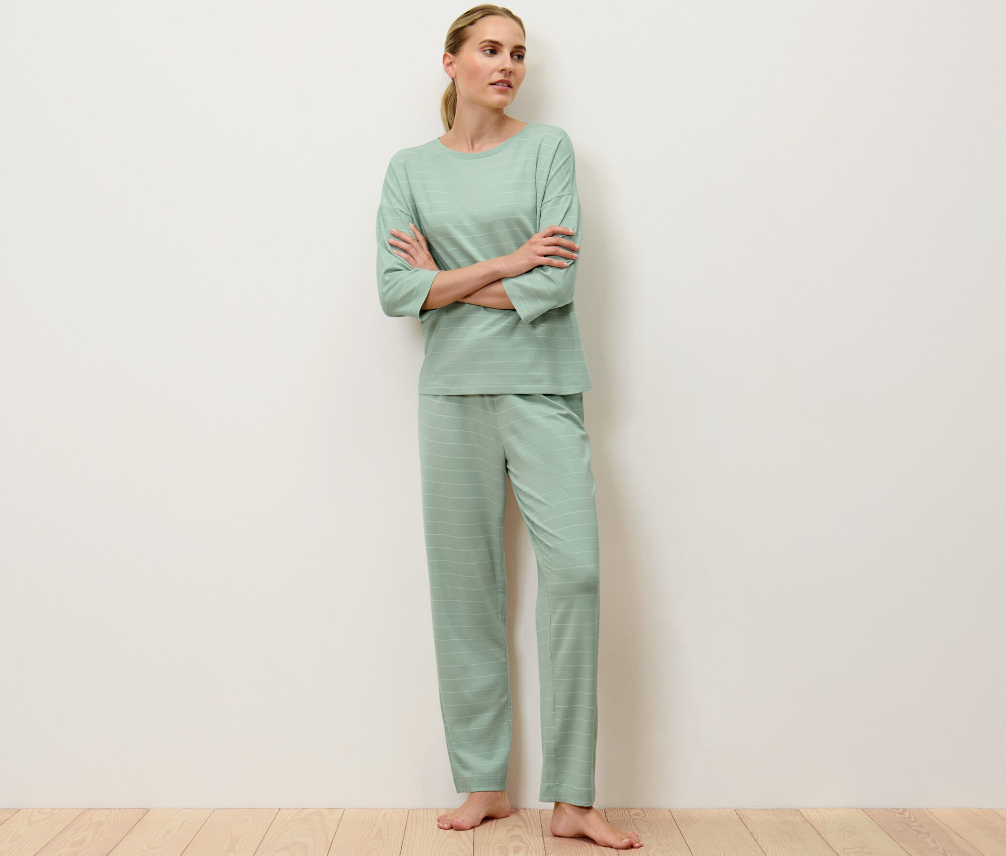 Frau steht mit verschränkten Armen da und trägt einen hellgrün gestreiften Pyjama.