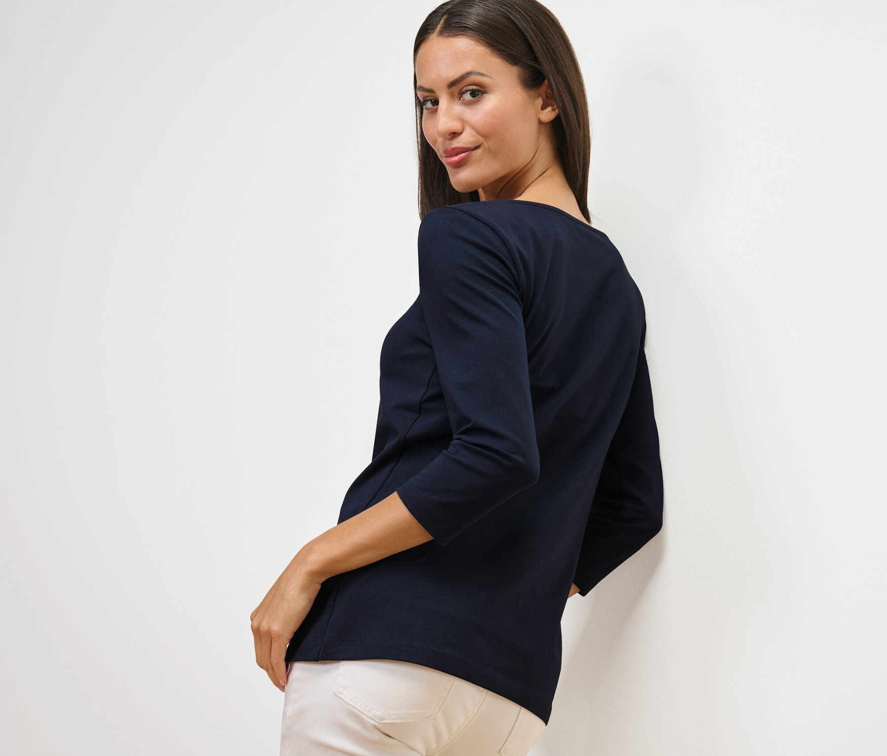 Frau blickt über die Schulter und trägt ein marineblaues Shirt mit 3/4-Arm.