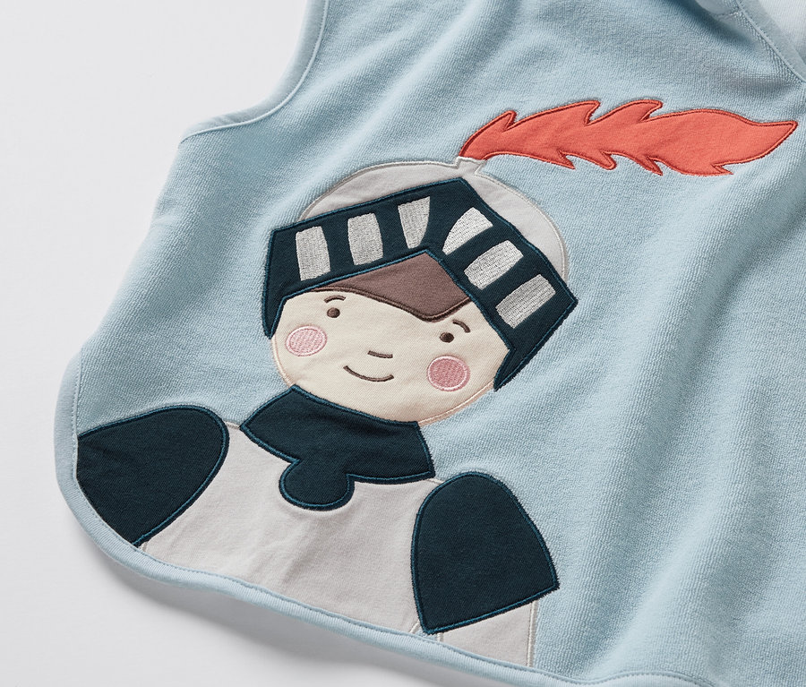 Detailansicht eines hellblauen Frottierponchos mit Ritter-Applikation.