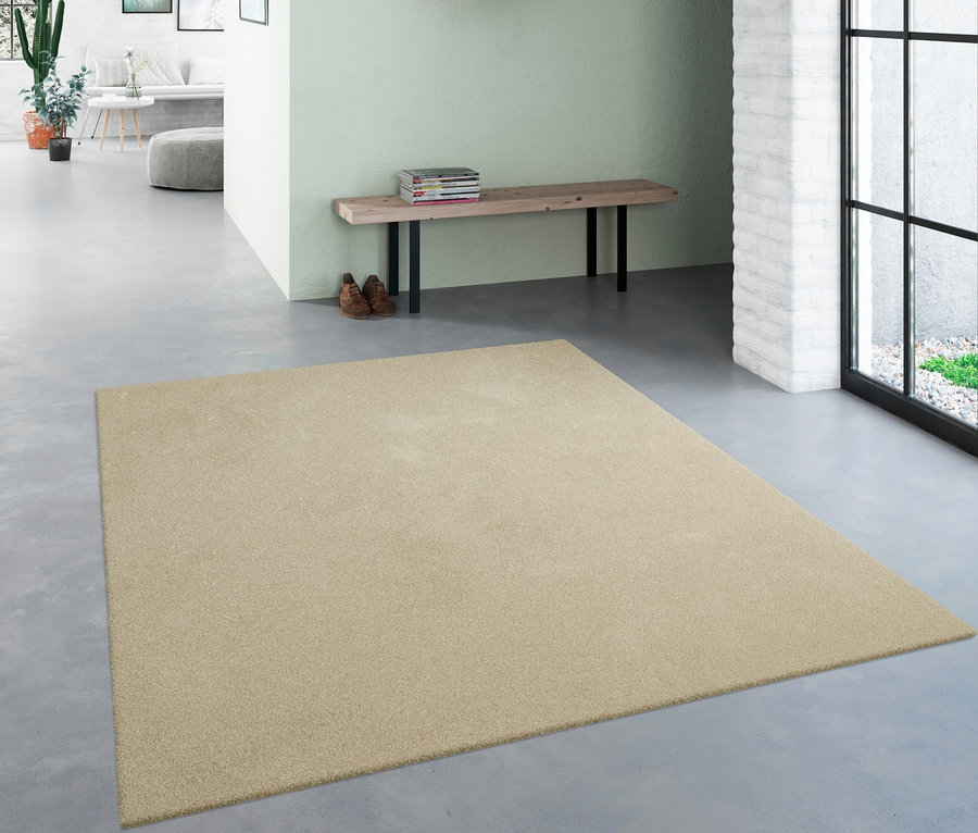 Ein beiger Teppich »Mellow« liegt in einem Flur. Darüber befinden sich ein Spiegel und eine Bank.