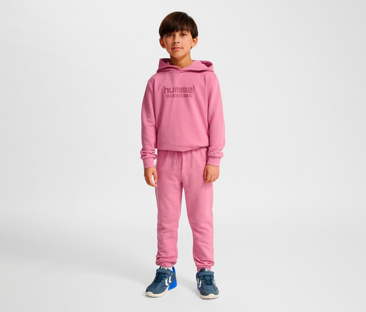 Junge steht und trägt ein rosa HUMMEL HMLJR Base Regular Pants Set.
