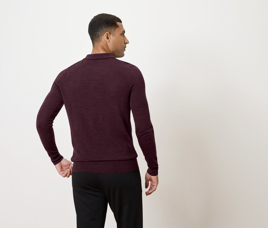 Mann in burgunderfarbenem Langarmpullover und schwarzer Hose, der nach links schaut.