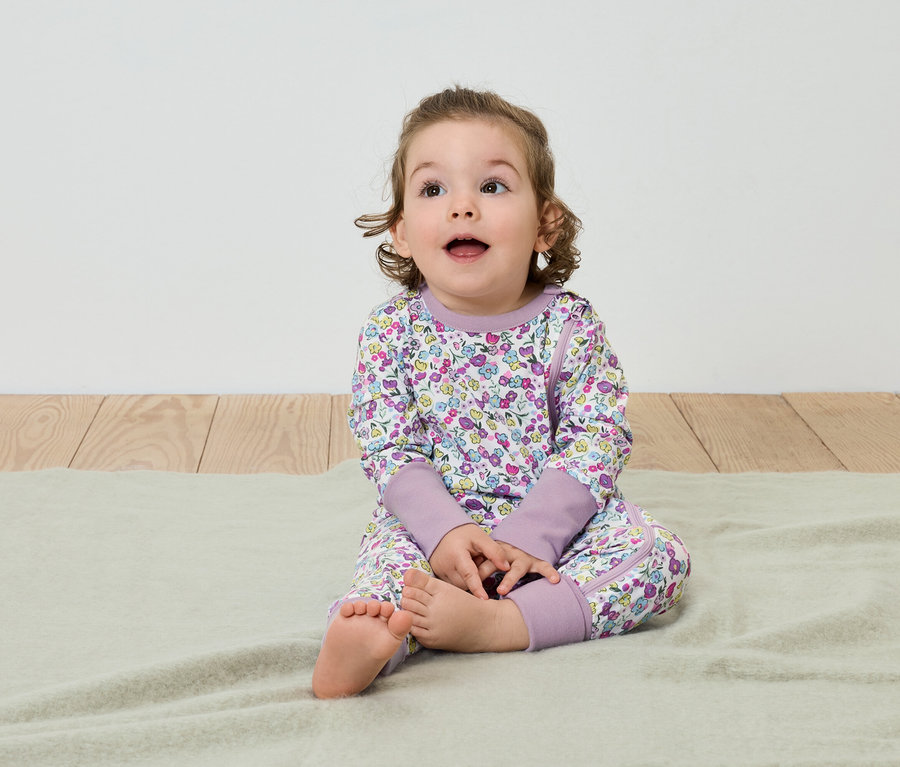 Ein Kind sitzt auf einer Decke und trägt einen Schlafanzug mit Blumenmuster.