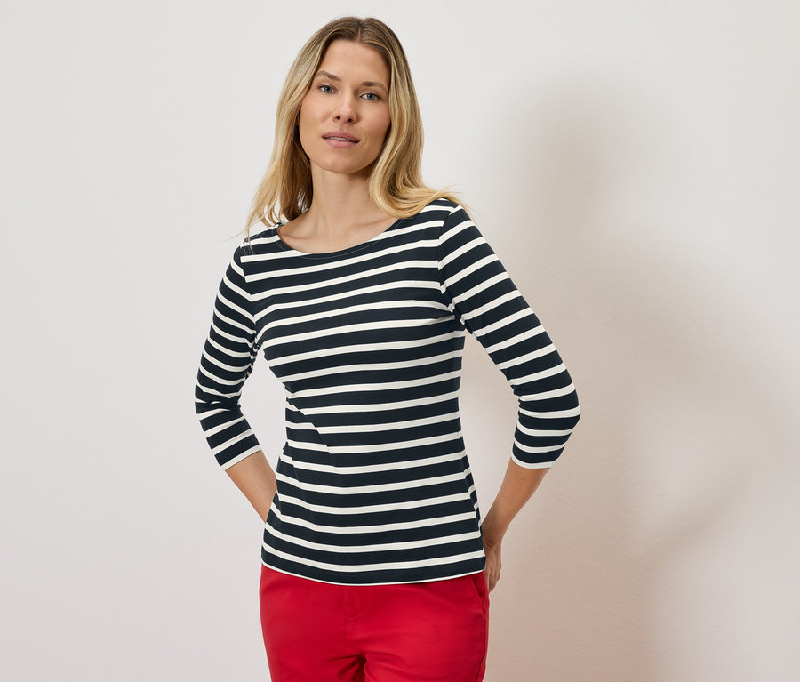 Blonde Frau trägt ein gestreiftes Dreiviertelarmshirt und rote Hosen.