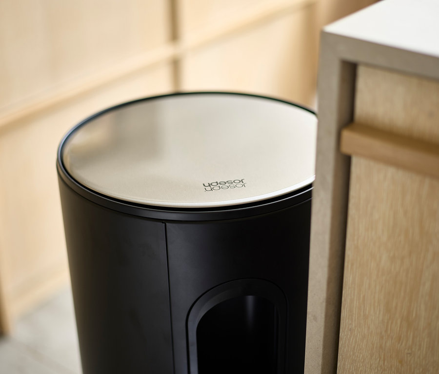 Detailansicht eines schwarzen Joseph Joseph Abfalleimers mit cremefarbenem Deckel neben einem Holzschrank.