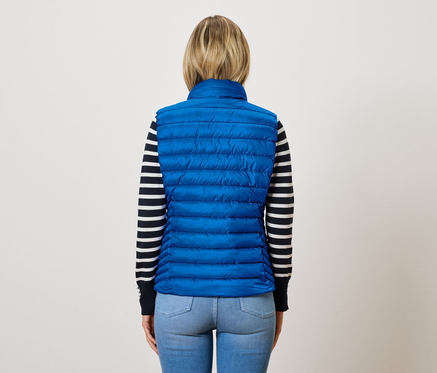 Frau von hinten trägt eine blaue Steppweste über einem gestreiften Pullover.