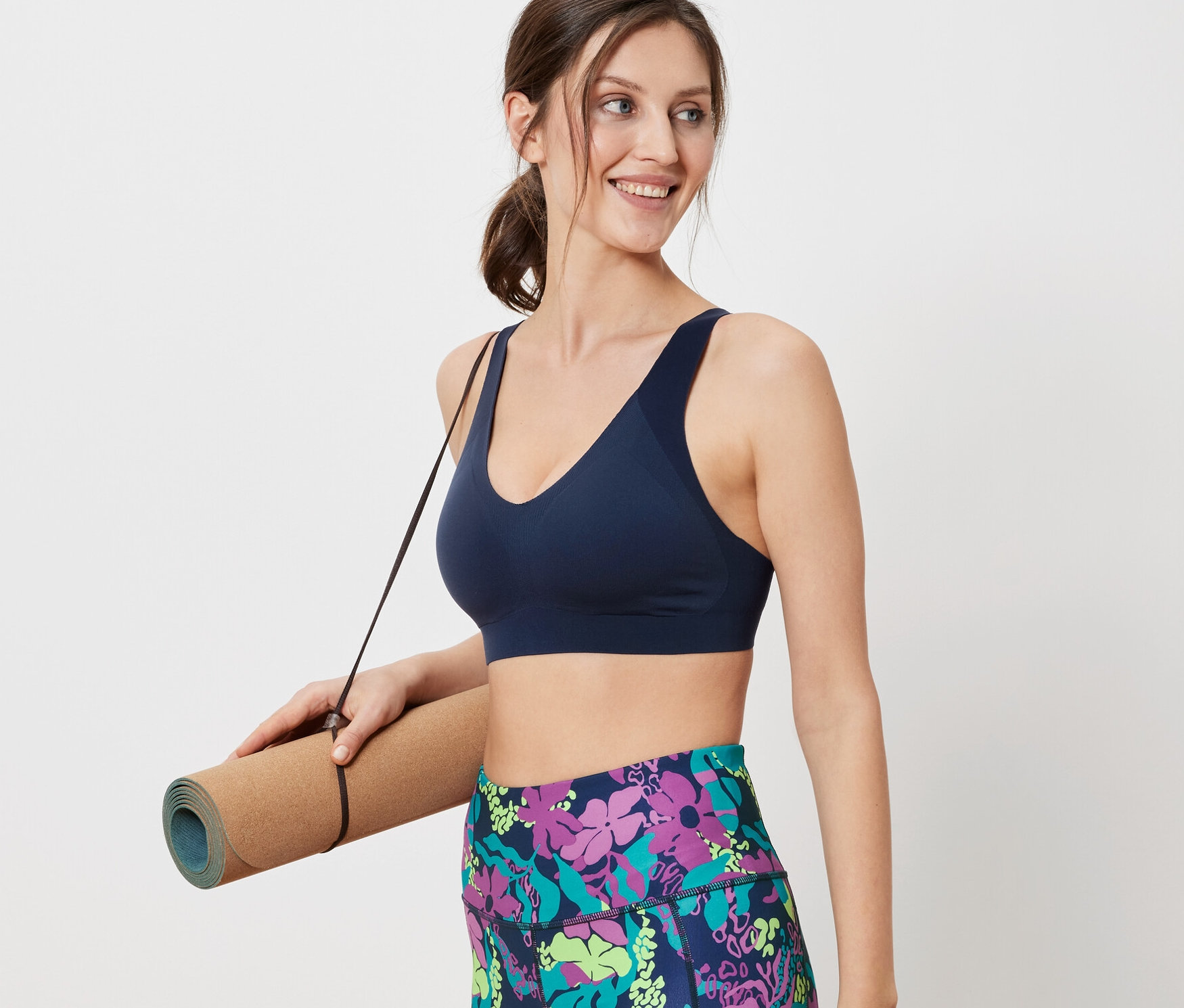 Frau hält eine Yogamatte und trägt einen Sport-BH.