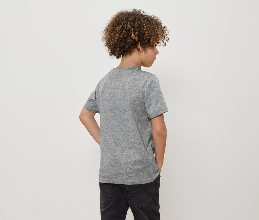 Junge mit lockigem Haar steht mit dem Rücken zur Kamera und trägt ein graues T-Shirt und schwarze Jeans.