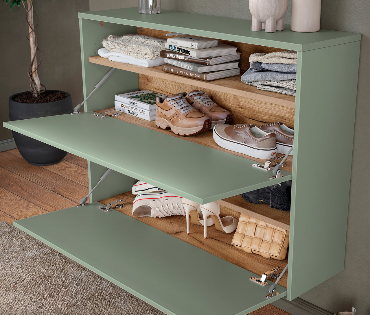 Hellgrüner Schuhschrank mit zwei offenen Klappen, gefüllt mit Schuhen, Büchern und Kleidung.