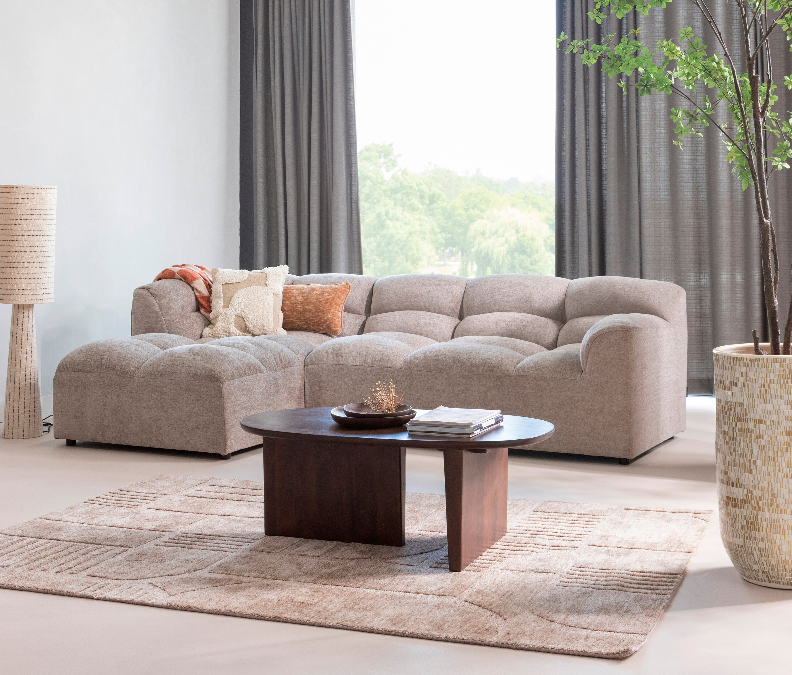 Wohnzimmer mit beigem Modulsofa, dunklem Couchtisch, gemustertem Teppich und Stehlampe.