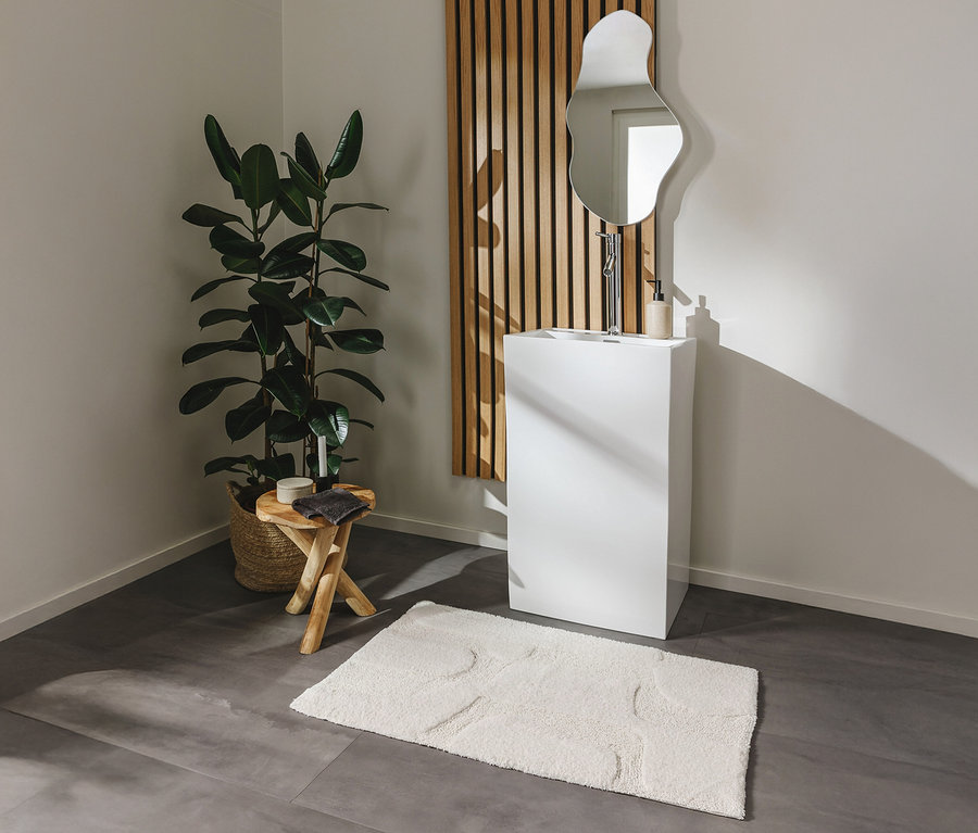 Ein Badezimmer mit einem weißen Waschtisch, einem Spiegel und einer Zimmerpflanze. Auf dem Boden liegt eine weiße Badematte »Nehir« von benuta in der Größe 60 x 100 cm.