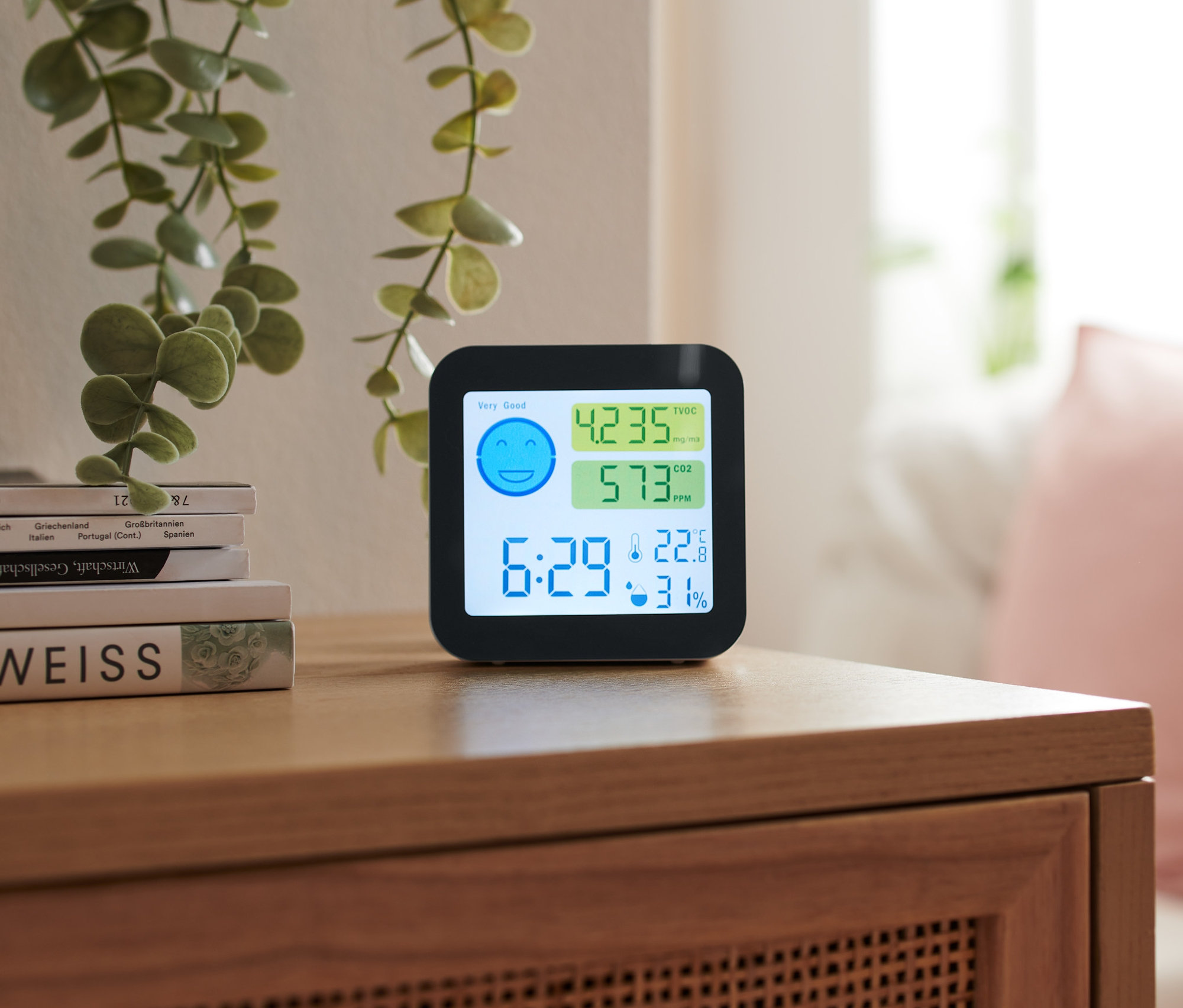 Ein Luftgüte-Sensor steht auf einem Holzschrank neben Büchern.