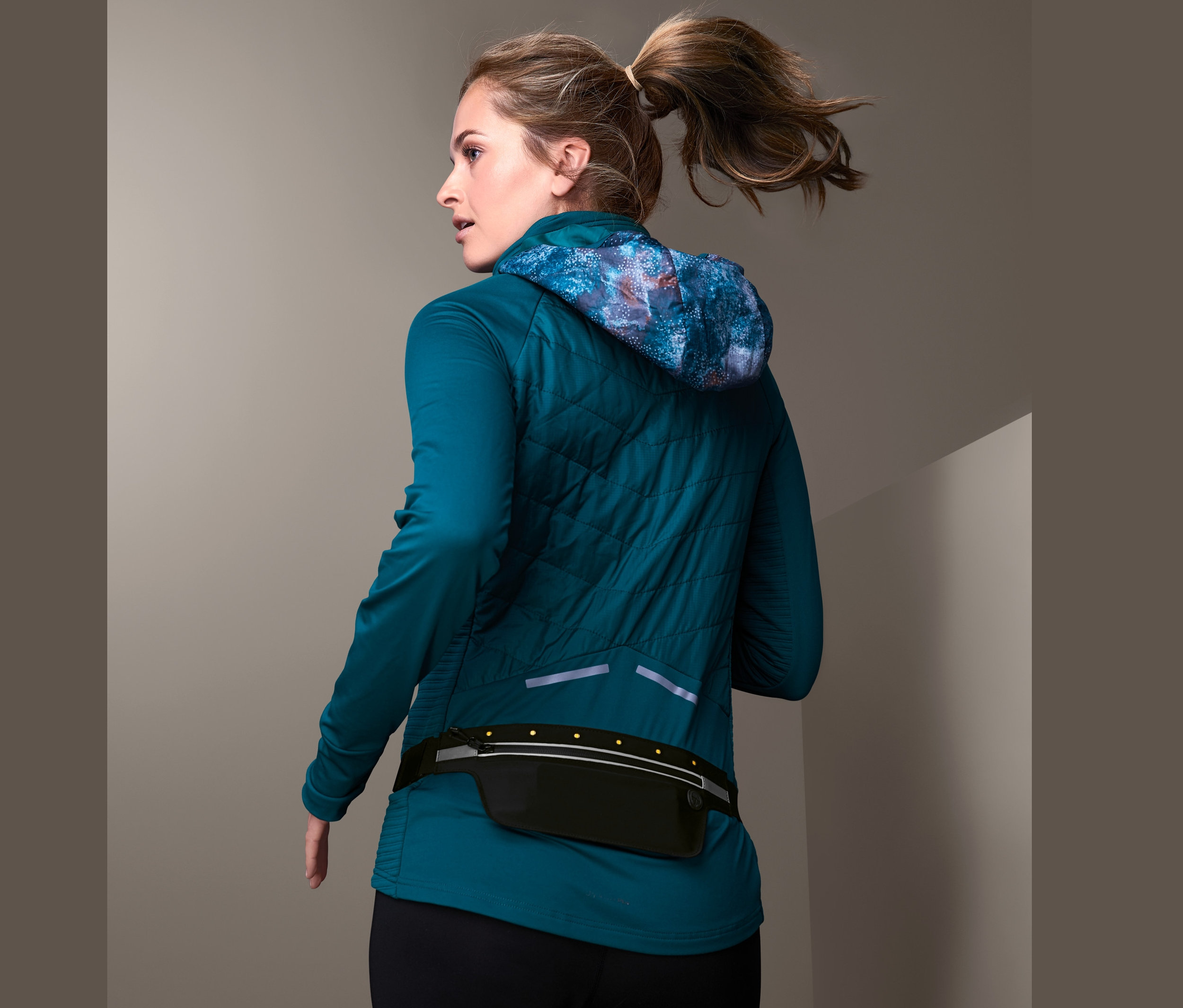 Blonde Frau mit Pferdeschwanz trägt einen schwarzen LED-Laufgürtel für Smartphones.