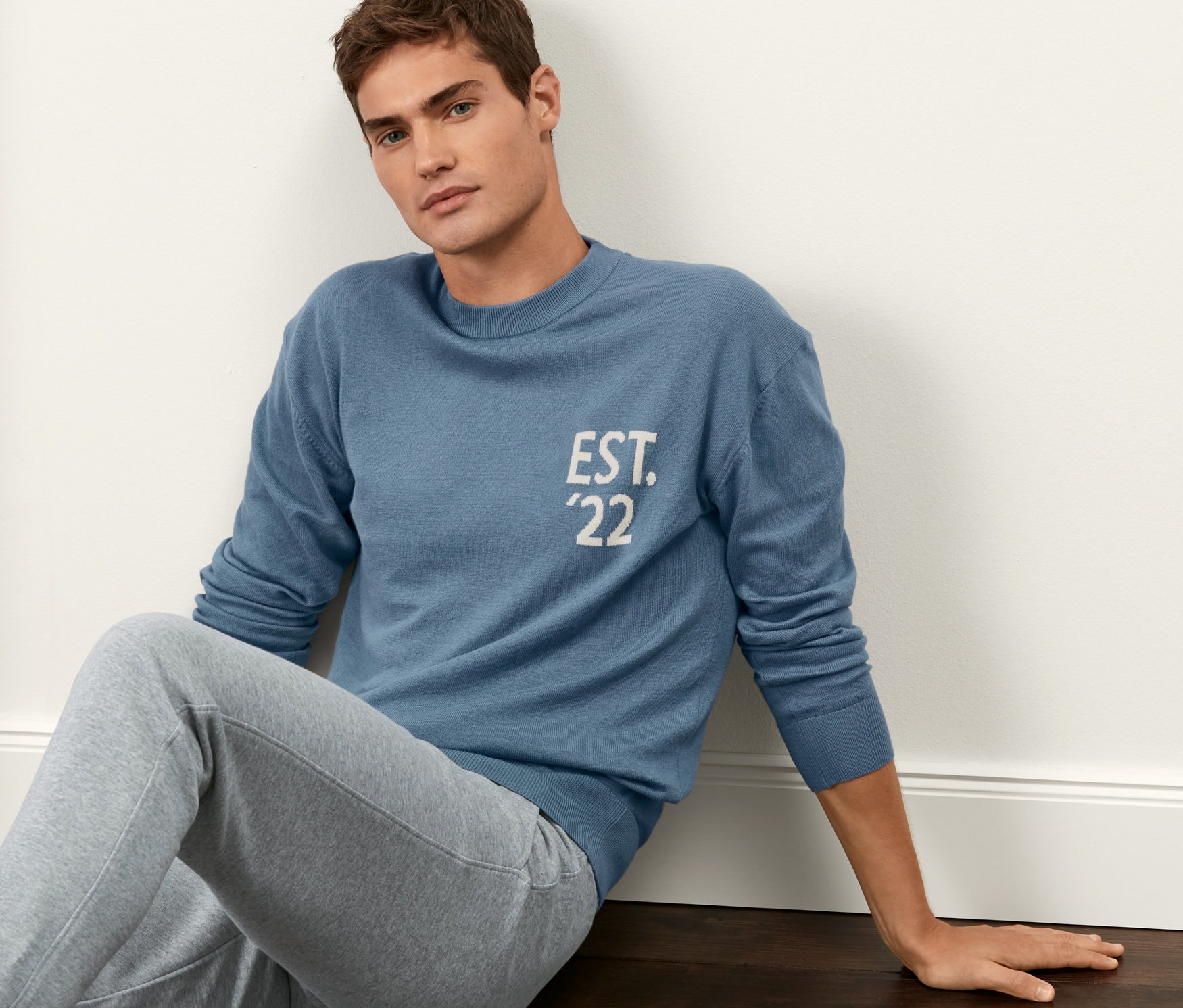 Mann sitzt auf dem Boden und trägt einen blauen Pullover.