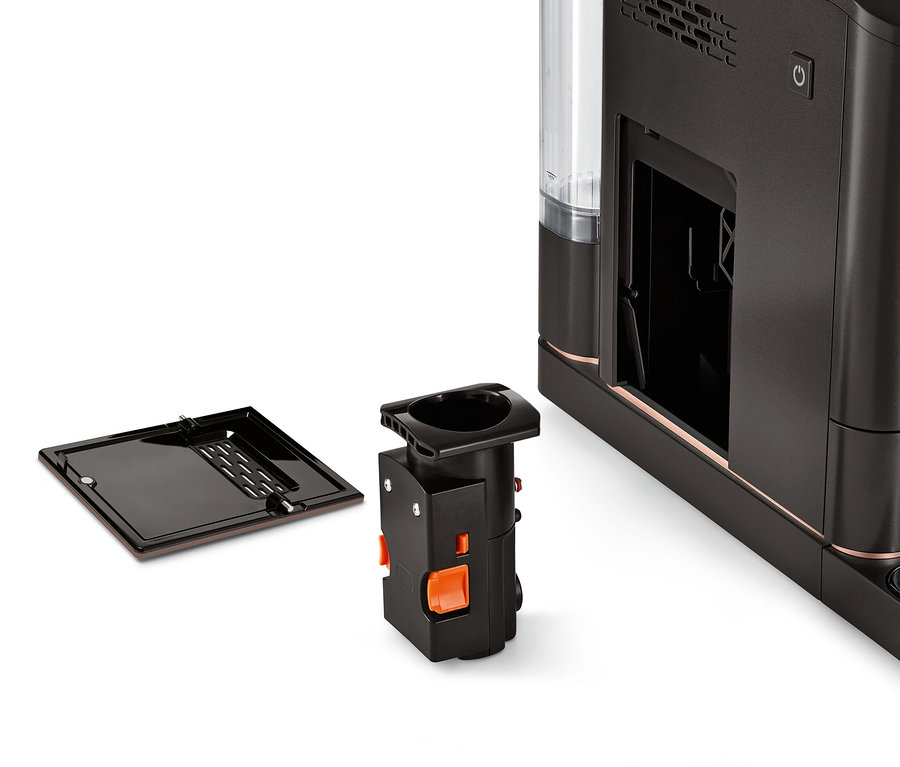 Eine Brühgruppe für Tchibo Vollautomaten liegt neben einer Kaffeemaschine.