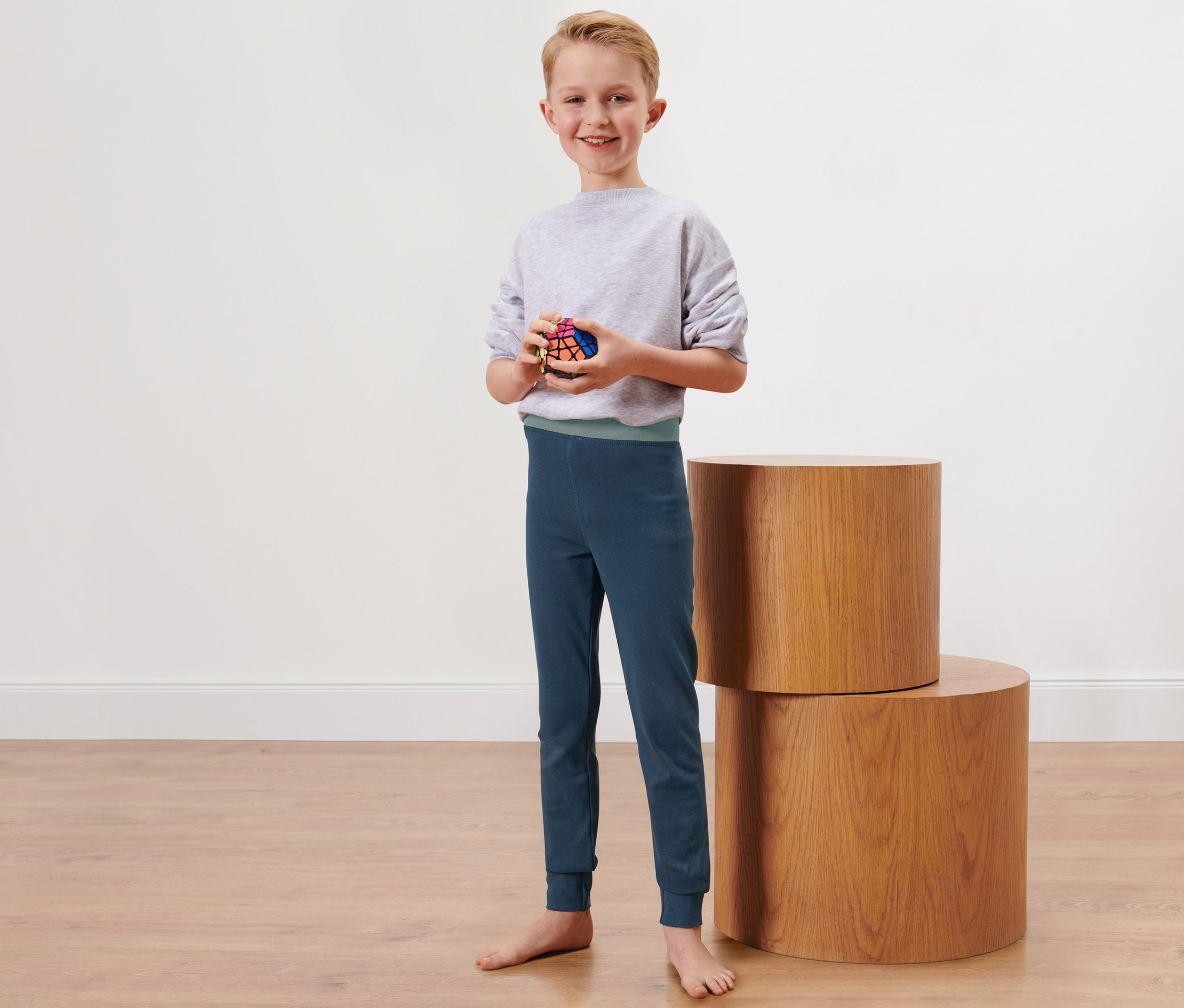 Ein Junge steht barfuß da und hält einen Zauberwürfel. Er trägt eine lange Kinder-Winterunterhose.