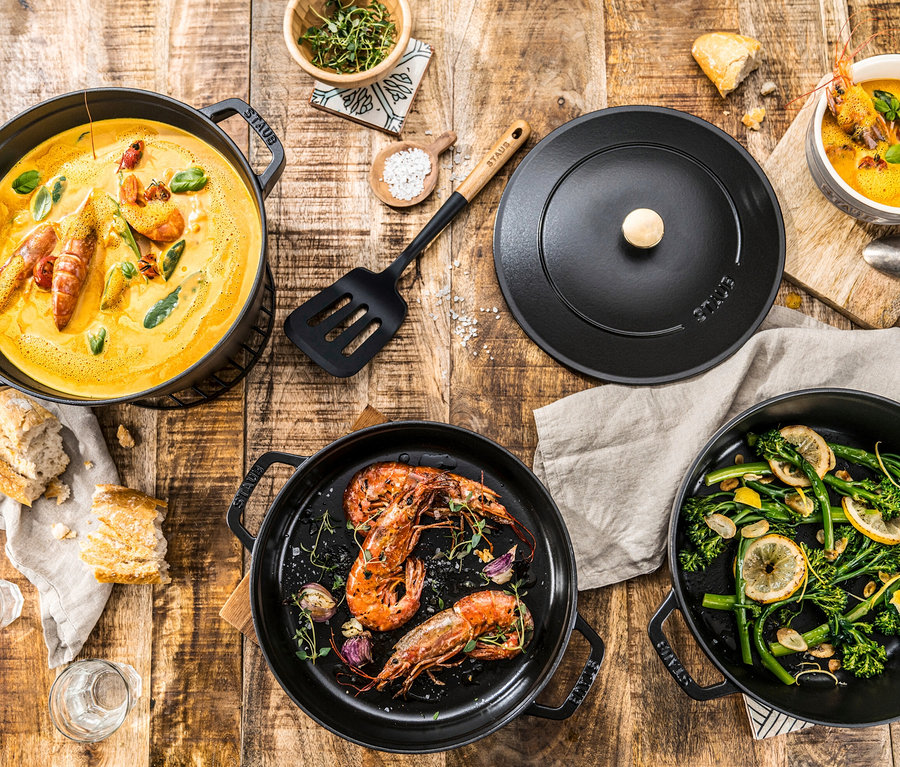 Speisen in Staub Gusseisen-Kochtopf-Sets auf einem Holztisch.