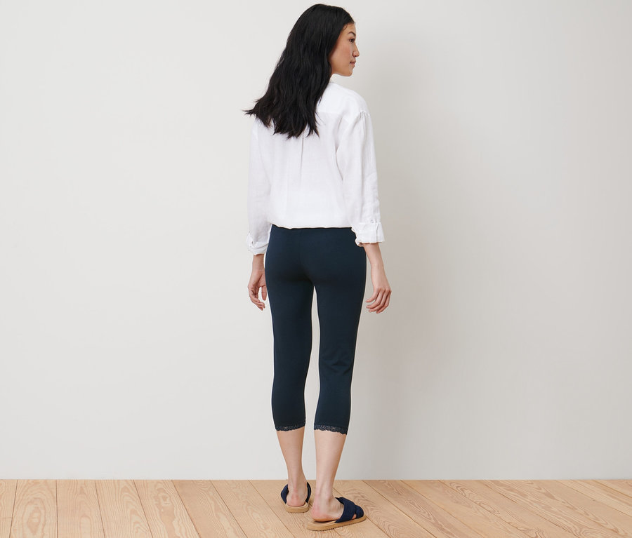 Eine Frau steht mit dem Rücken zur Kamera und trägt eine dunkelblaue 3/4-Leggings mit Spitzenborte.