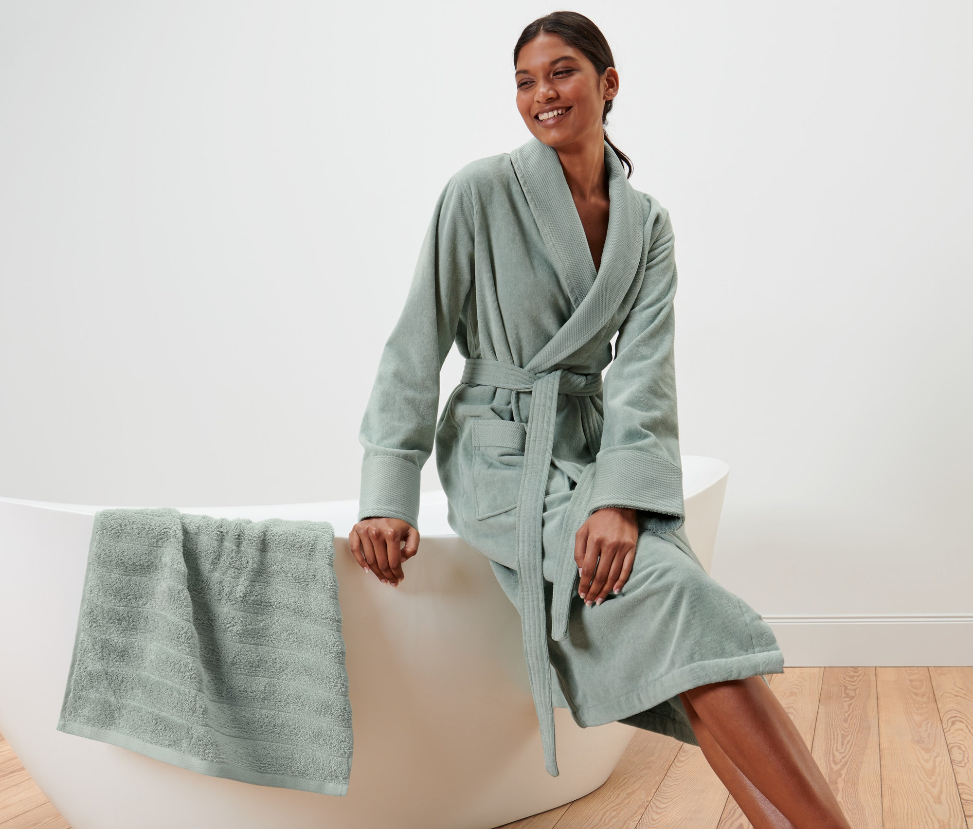 Frau sitzt auf Badewannenrand und trägt Damen-Velours-Bademantel.
