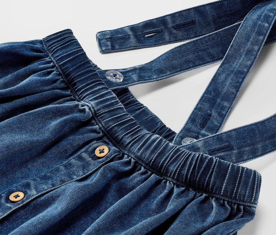 Detailaufnahme eines Kleinkind-Denimrocks mit Trägern und Knöpfen.