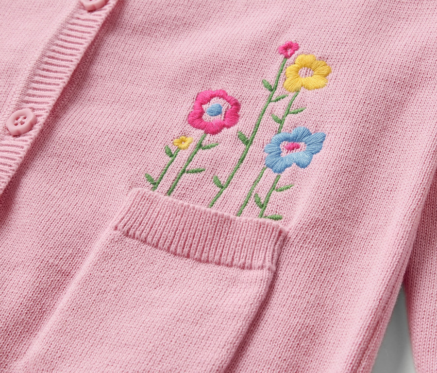 Detail einer Baby-Strickjacke in Rosa mit Blumenstickerei und Knöpfen.