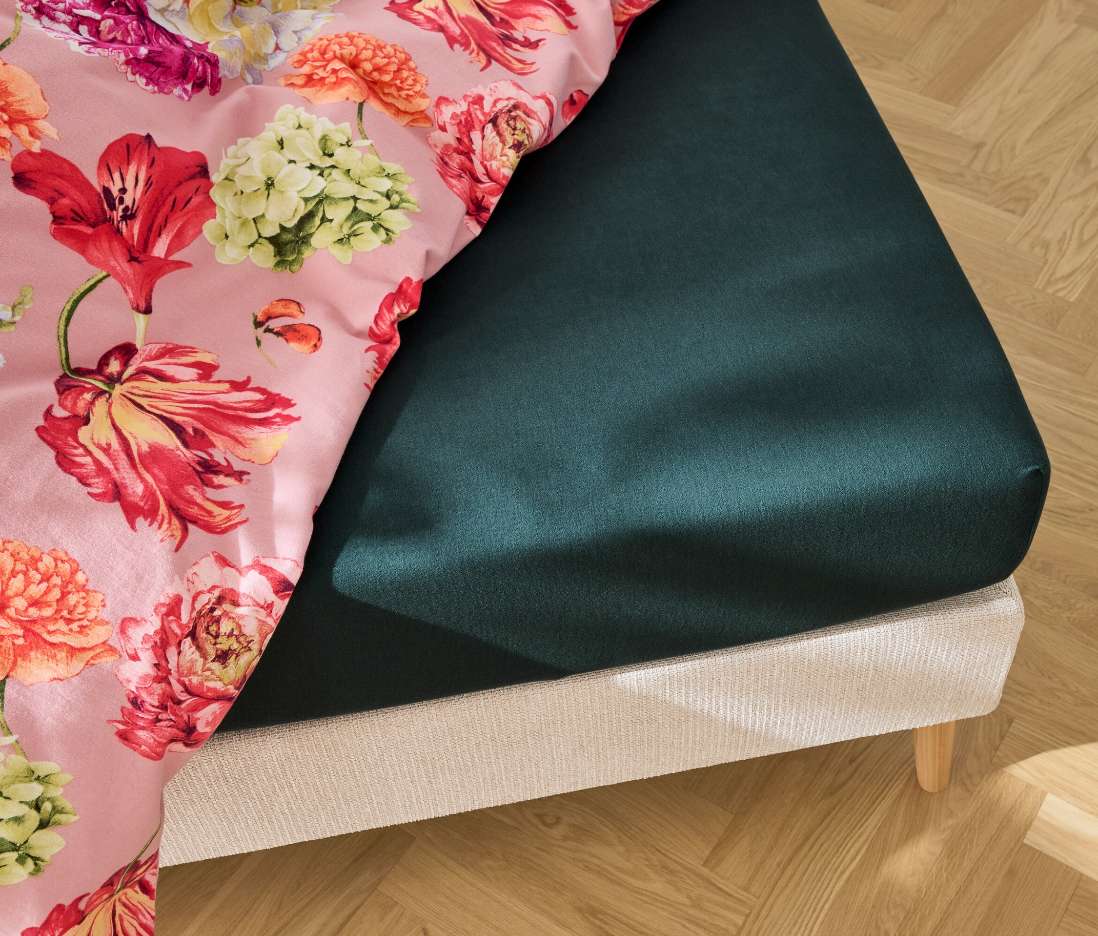 Detailansicht eines Bettes mit einem dunkelgrünen Spannbettlaken und Bettwäsche mit Blumendruck.