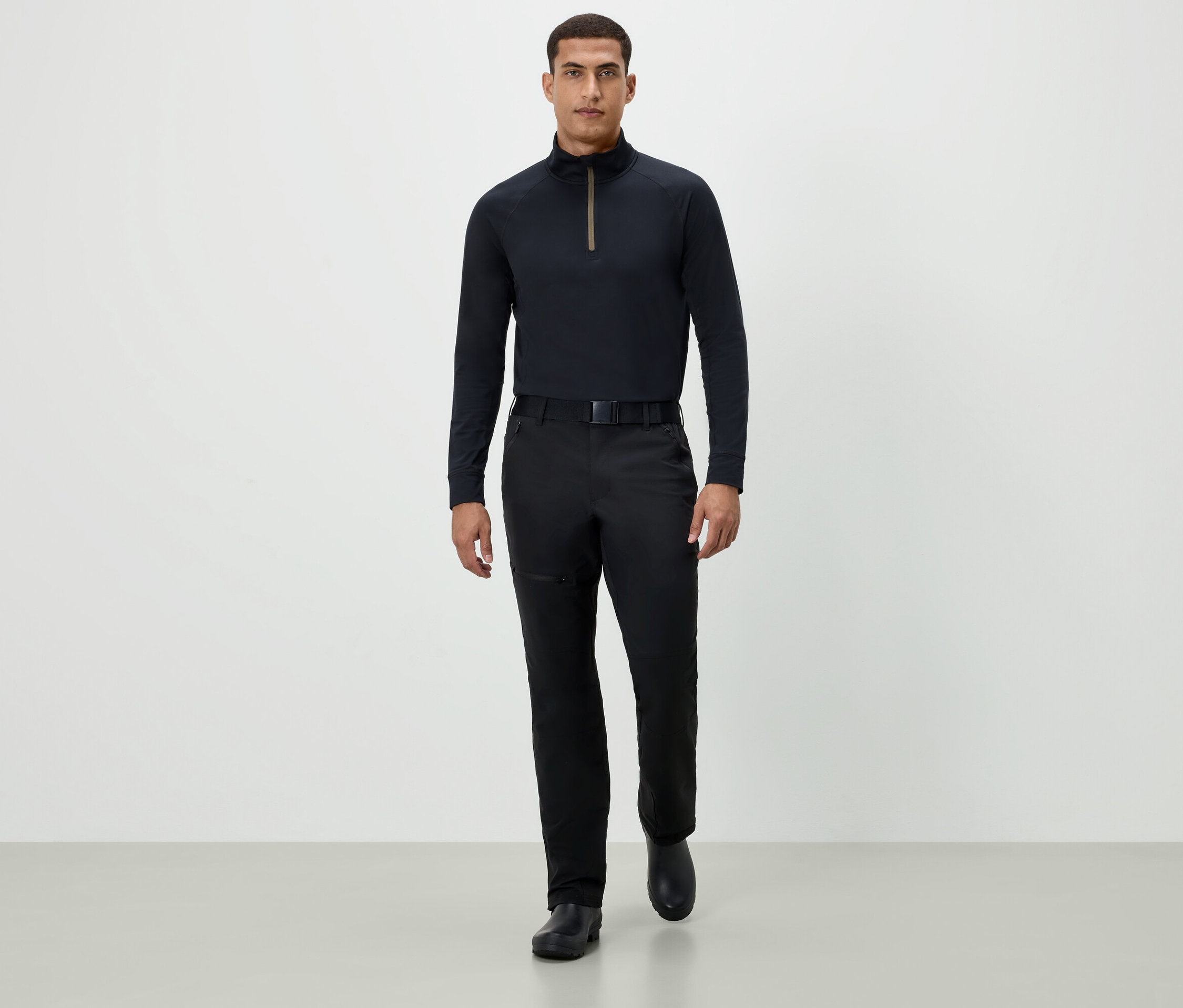 Ein Mann geht in einem schwarzen Langarmshirt, schwarzen Hosen und schwarzen Schuhen vorwärts.