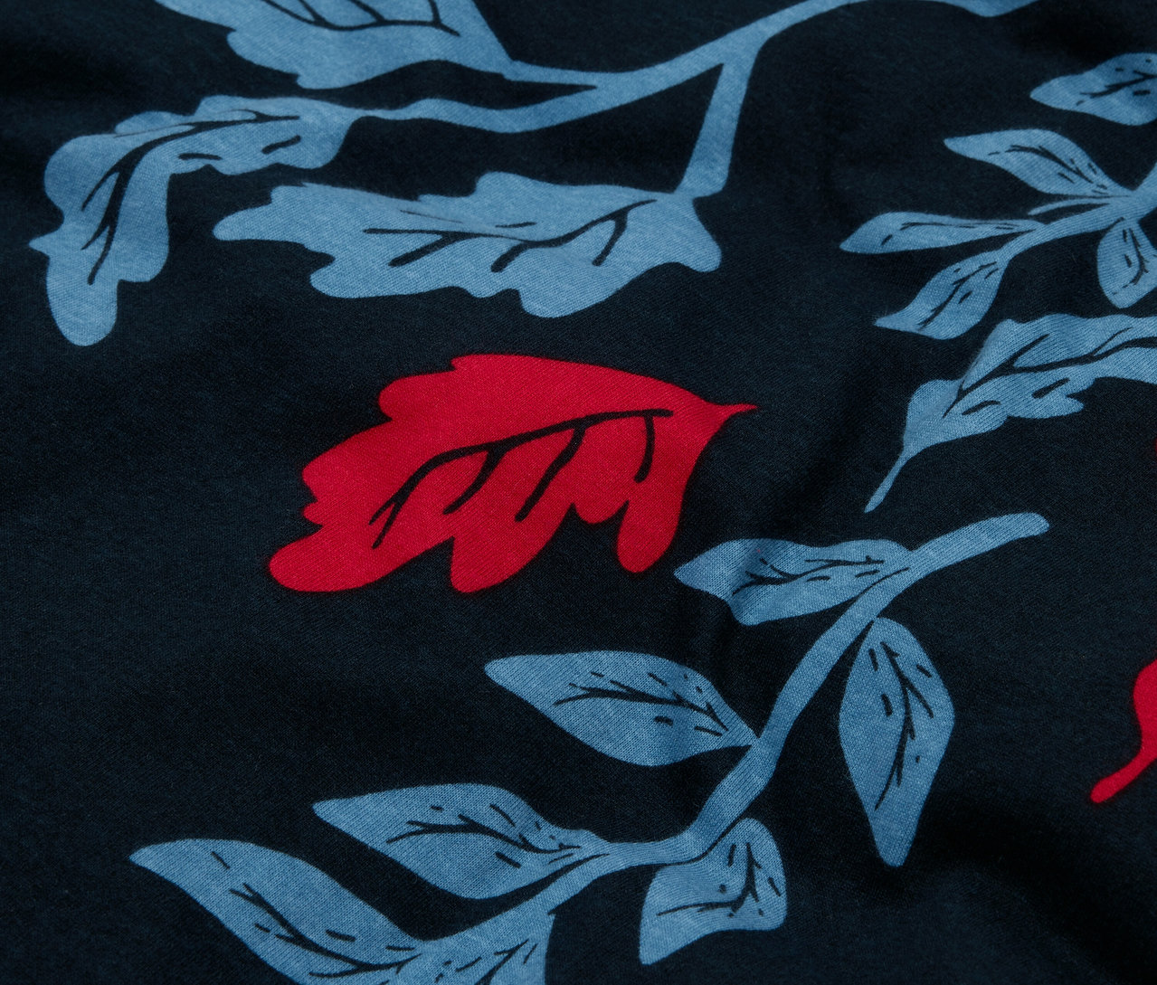 Detailaufnahme eines marineblauen Stoffes mit einem Allover-Muster aus blauen Blättern und roten Akzenten.