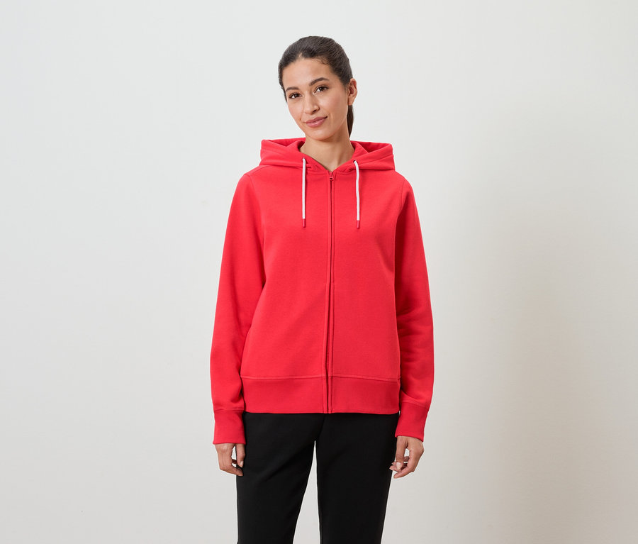 Eine Frau trägt einen roten Kapuzenpullover und eine schwarze Hose.