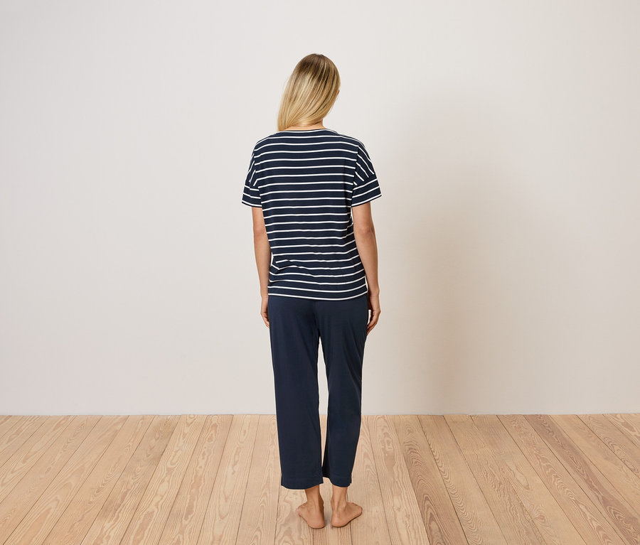 Rückansicht einer Frau mit blonden Haaren, die ein blau gestreiftes T-Shirt und eine blaue Hose trägt.