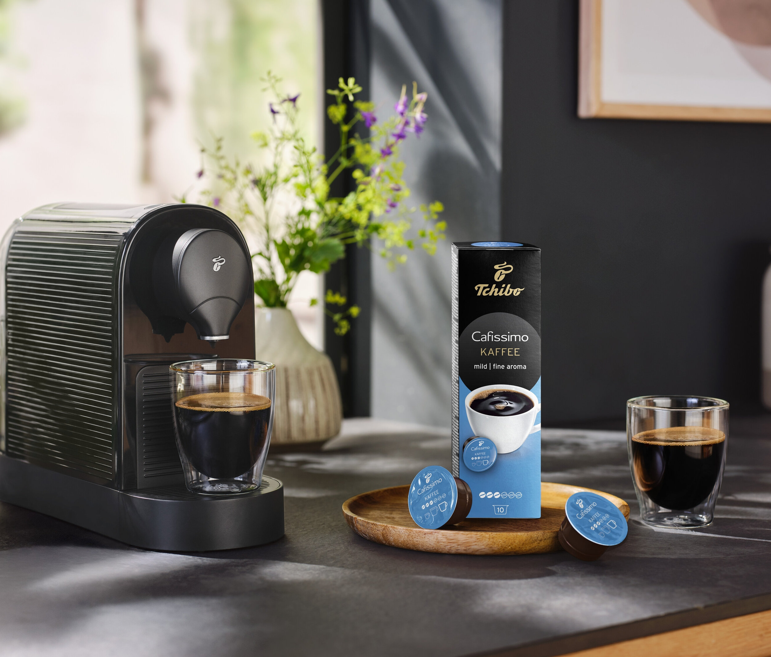 Kaffeemaschine steht neben einem Glas Kaffee und einer Packung Cafissimo Kaffee mild - 10 Kapseln.