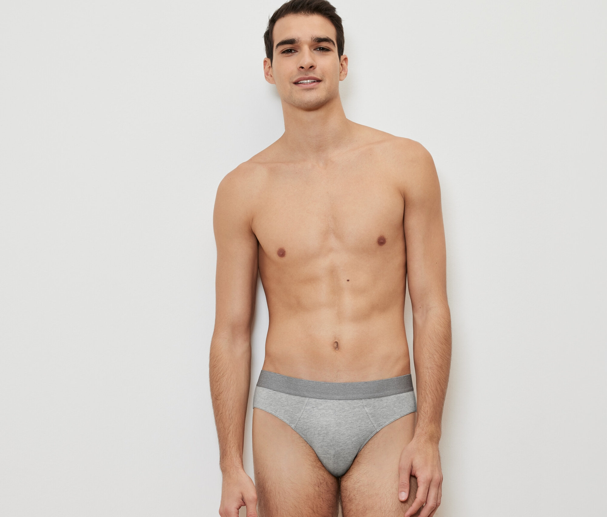 Mann posiert vor einem weißen Hintergrund und trägt einen grauen Slip aus einem 4er-Pack.