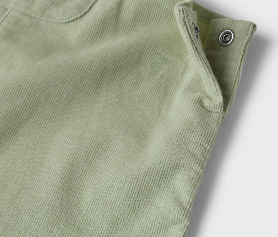 Detailaufnahme eines hellgrünen Cordstoffes mit Knopfverschluss.