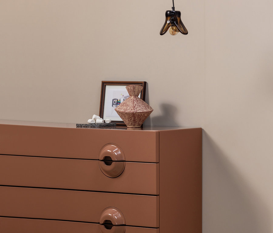 Braune WOOOD Kommode »Merge« mit Deko und Lampe vor beiger Wand.